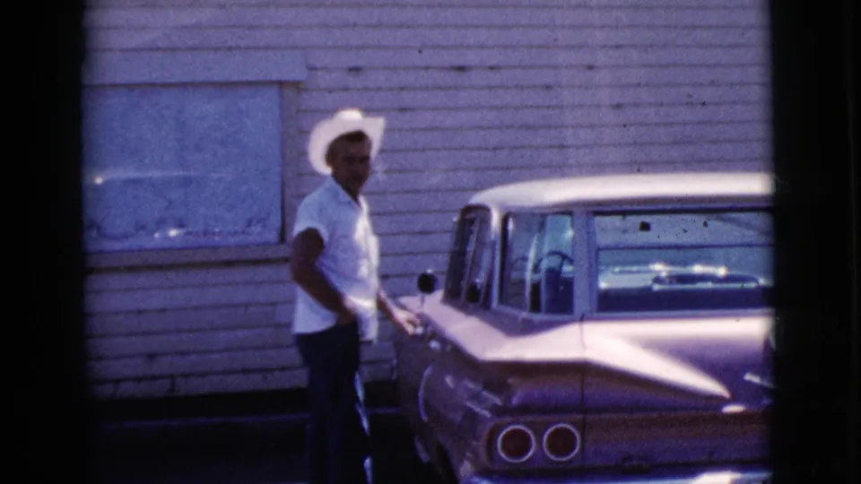 The man turns toward the camera or someone nearby while standing beside the vintage sedan in the Cottonwood, Arizona street-side scene.