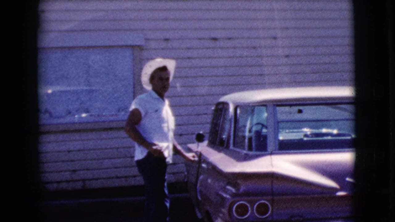 Man in a white cowboy hat beside a vintage station wagon near a wooden building.