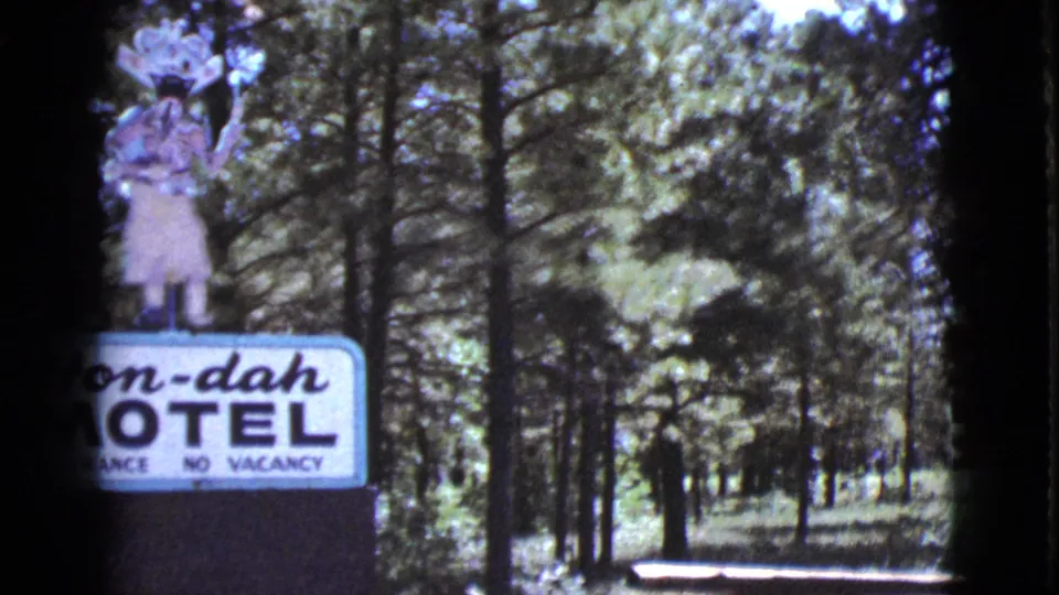 Cottonwood motel sign topped by a Native American figure, with vacancy text, trees, and shaded grounds visible behind it.