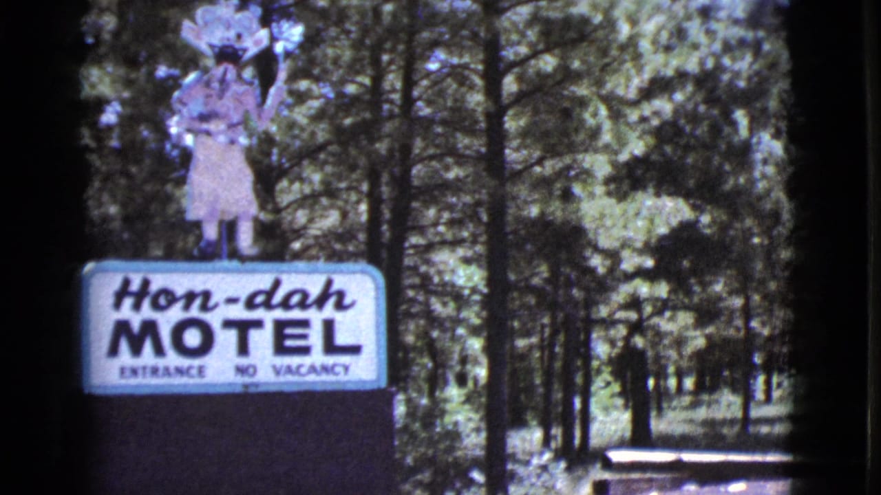 Hon-dah Motel sign standing among pine trees near a road.