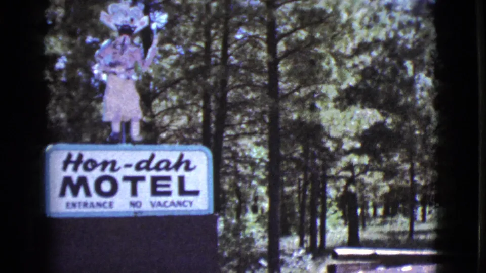 1964 Arizona home-movie frame showing the Hon-dah Motel entrance sign in a wooded pine setting.