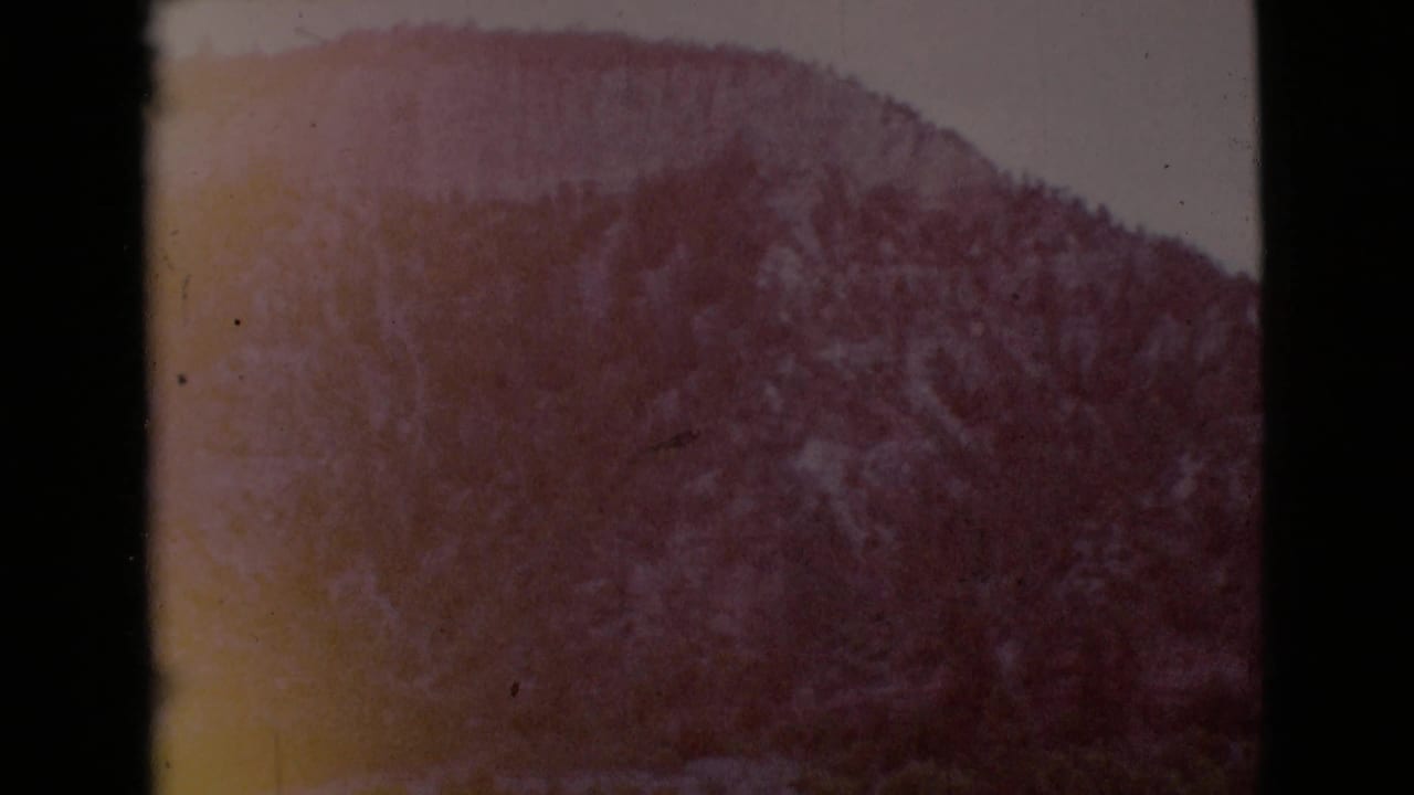 Soft, reddish view of a long mountain slope bordered by dark film edges.