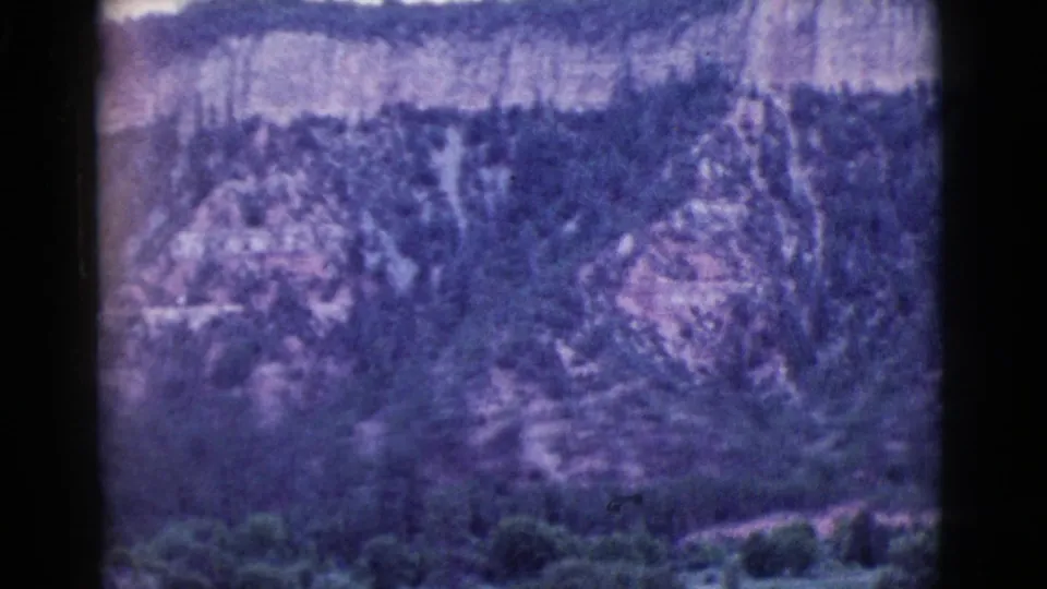 Cottonwood, Arizona landscape frame showing a rocky wooded hillside and foreground brush in soft, grainy 1960s 8mm color.