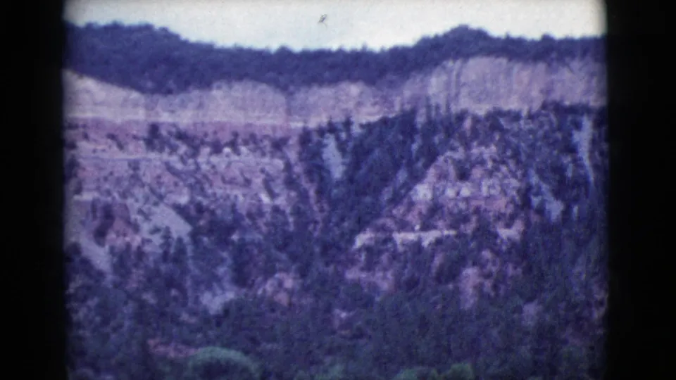 Wide 1964 Cottonwood, Arizona home-movie view of wooded hills, a pale distant ridge, and bright sky with visible 8mm aging.