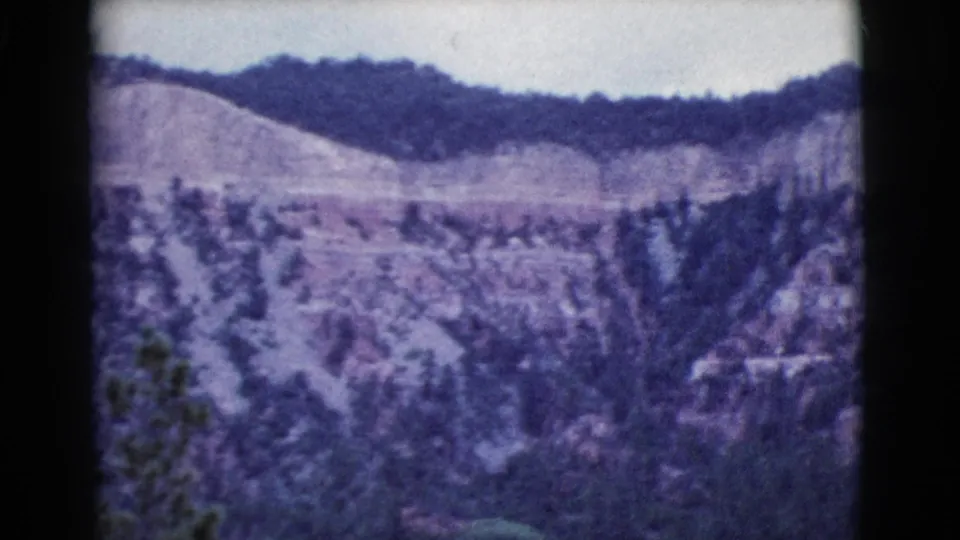 1964 Cottonwood, Arizona 8mm frame showing rocky layered slopes, scattered trees, and a pale overcast sky.