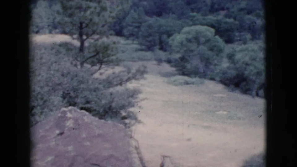 1964 Cottonwood, Arizona 8mm frame showing a pale dirt field, green shrubs, scattered trees, and dark gate edges.