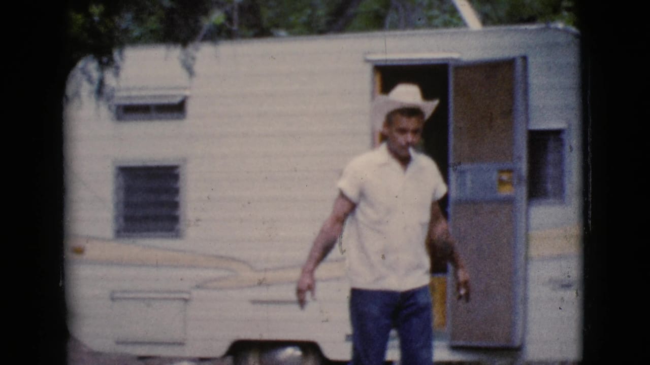 Man in a white cowboy hat walks in front of a light-colored camper trailer.