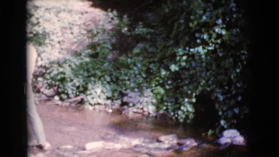 A man begins to enter the 1964 Cottonwood stream scene, partly cut off by the frame, with rocks and dense foliage behind him.