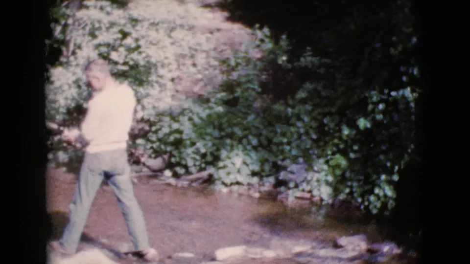 A man in a light sweater and trousers walks along the Cottonwood, Arizona stream bank in this soft 1964 8mm frame.