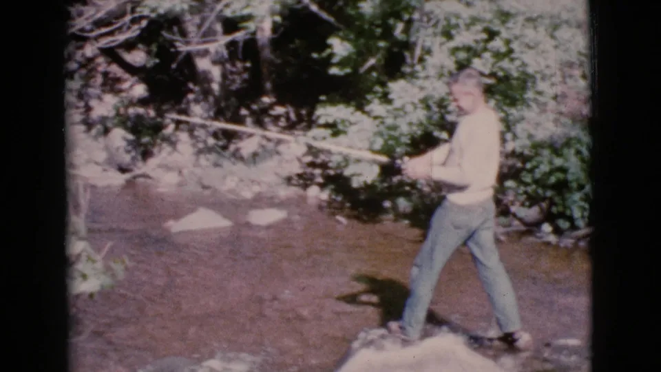 The closing frame shows the 1964 Cottonwood fisherman balanced on rocks in the shallow stream, rod angled toward the leafy bank.