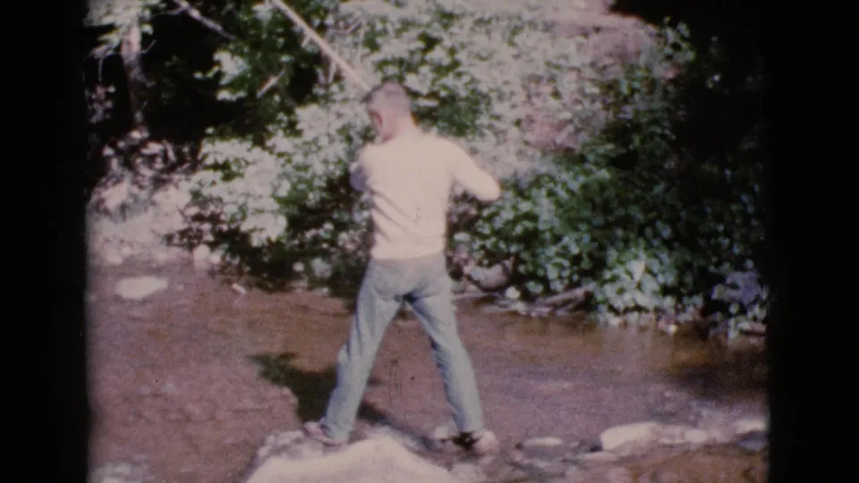 The home-movie frame shows the fisherman from behind as he casts across a shallow Arizona stream in 1964.