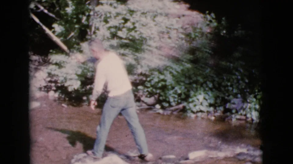 A man in jeans stands in the shallow Cottonwood stream after a cast, surrounded by rocks, water, and dense foliage.