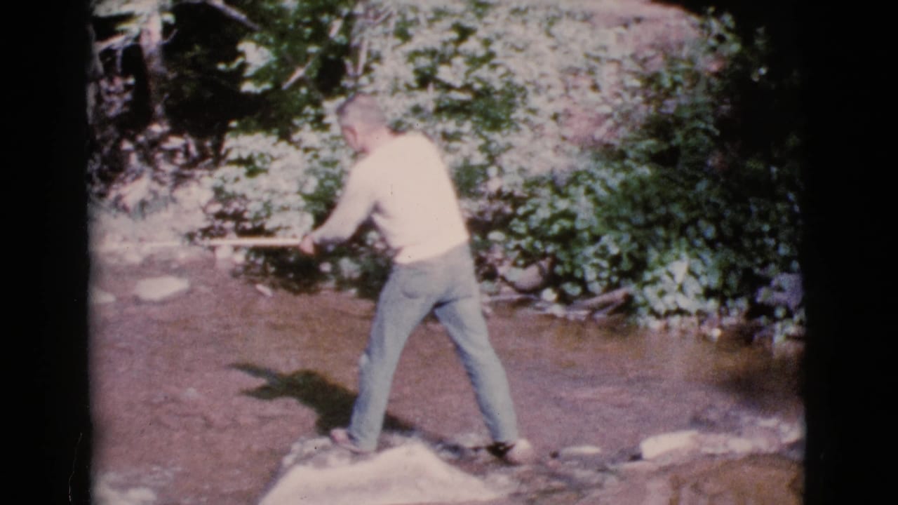 Man standing on a rock in a shallow creek while holding a fishing pole.