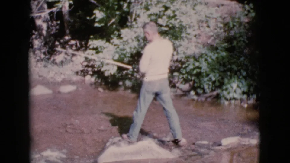 A home-movie frame shows the man from behind as he fishes in a shallow Cottonwood creek in 1964.