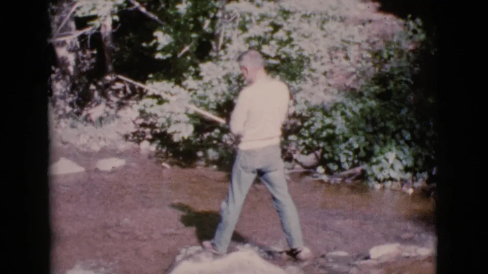 The final frame holds on the man fishing in a shallow creek bordered by dense green foliage in Cottonwood, Arizona.