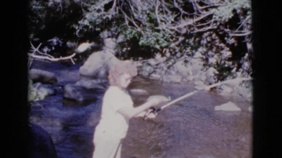 The woman appears to angle the fishing rod over the shallow stream in 1964 Cottonwood, Arizona home-movie footage.