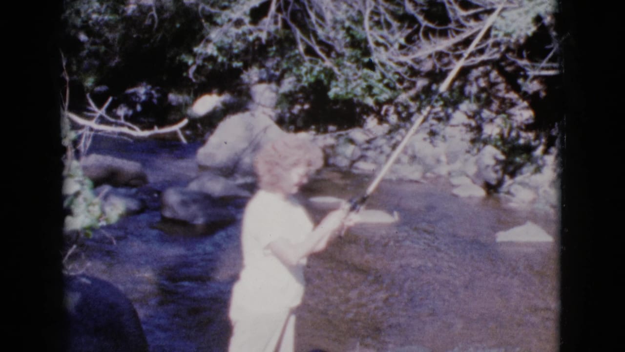 Woman raises a fishing rod while standing in the river near rocks.
