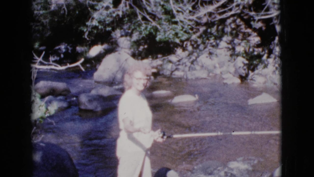 In 1964 Cottonwood, Arizona footage, a woman in light clothing stands near a rocky river while holding a fishing rod.