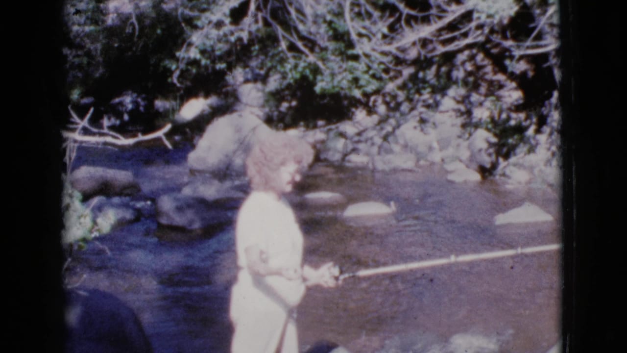 Woman in profile fishing beside a river with rocks and trees in the background.