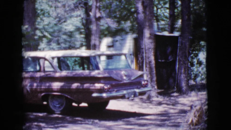1964 Cottonwood, Arizona home-movie frame showing a maroon station wagon parked beside trees at a wooded campsite.