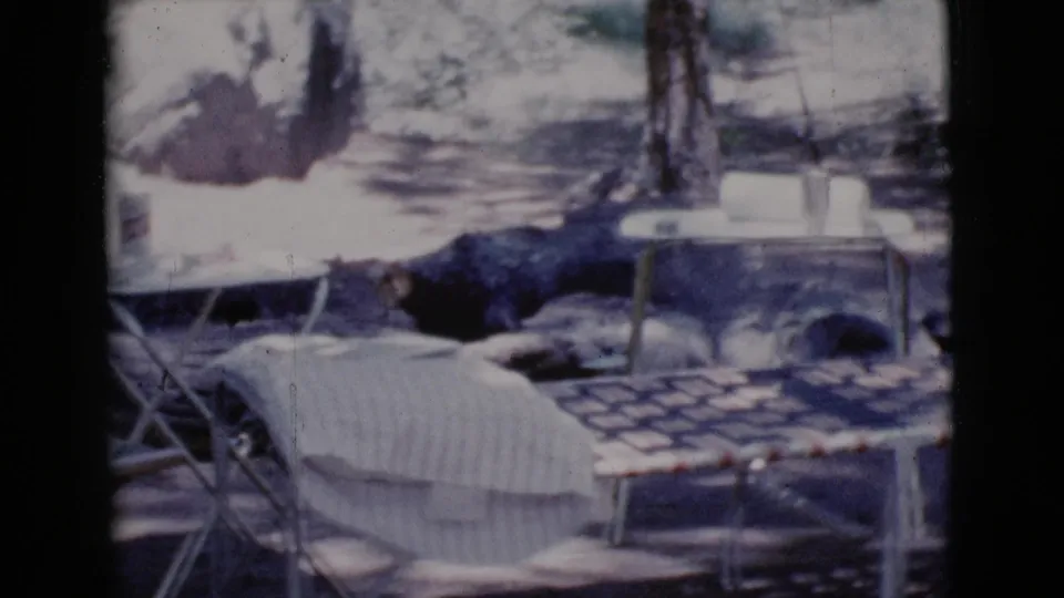 1964 Cottonwood, Arizona home-movie frame showing a picnic table, folding chairs, camper trailer, and shaded trees at a campsite.