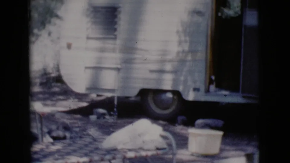 1964 Cottonwood, Arizona frame with a white camper trailer, open doorway, visible wheel, and campsite objects nearby.