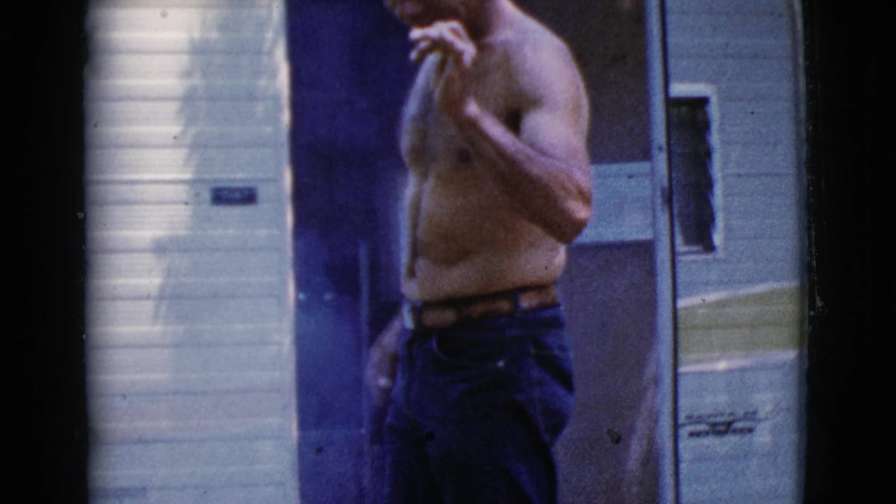 Shirtless man standing beside the open door of a tow camper.