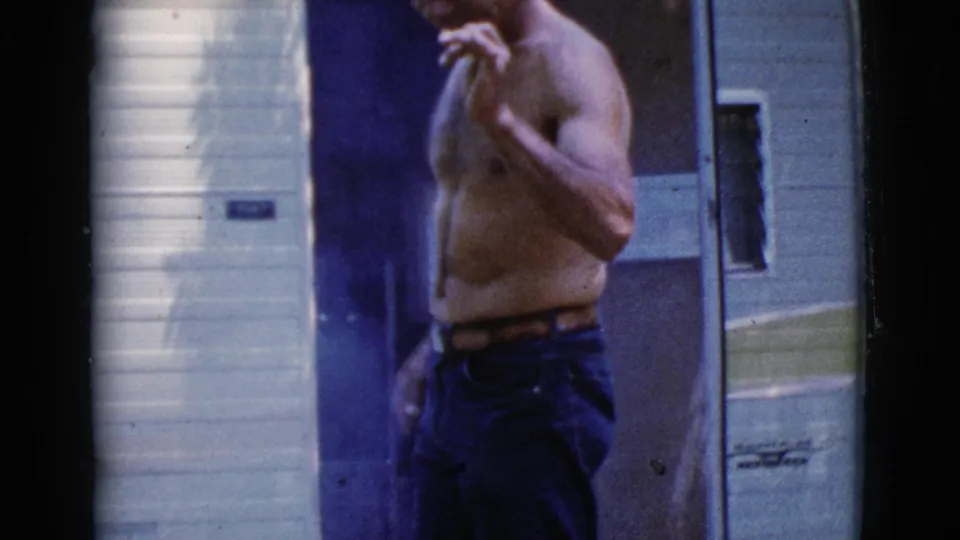 In Cottonwood, Arizona, a shirtless man stands near the doorway of a 1960s-era tow camper in soft 8mm home-movie footage.