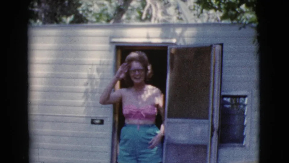 The woman smiles from the camper doorway, framed by pale trailer siding and the open screen door in Cottonwood, Arizona.
