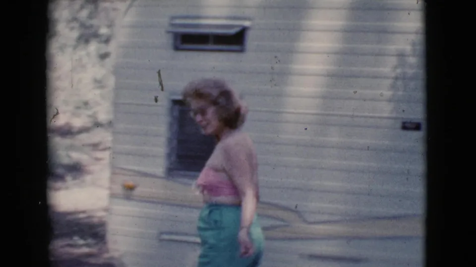 In Cottonwood, Arizona home-movie footage from 1964, a woman walks near a camper in a wooded area.