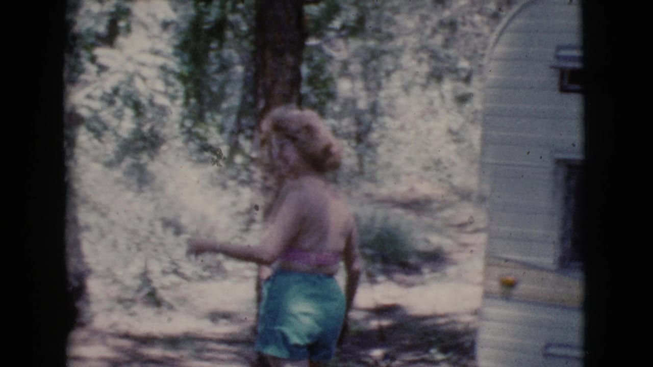 Woman walking past trees near the side of a camper.