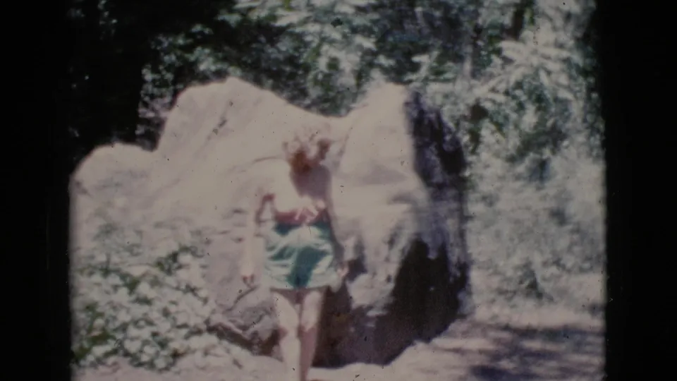 Soft 8mm frame showing the woman shifting beside the boulder on a sunny wooded trail near Cottonwood, Arizona.