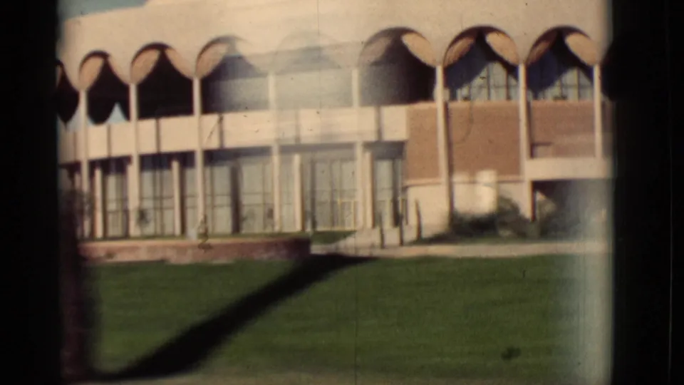 1964 New Mexico 8mm frame showing a modern building with repeated arches, glass bays, and lawn from a moving car.