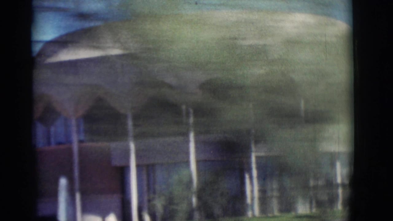 Blurred roadside view of a modernist building with arches seen through a vehicle window.