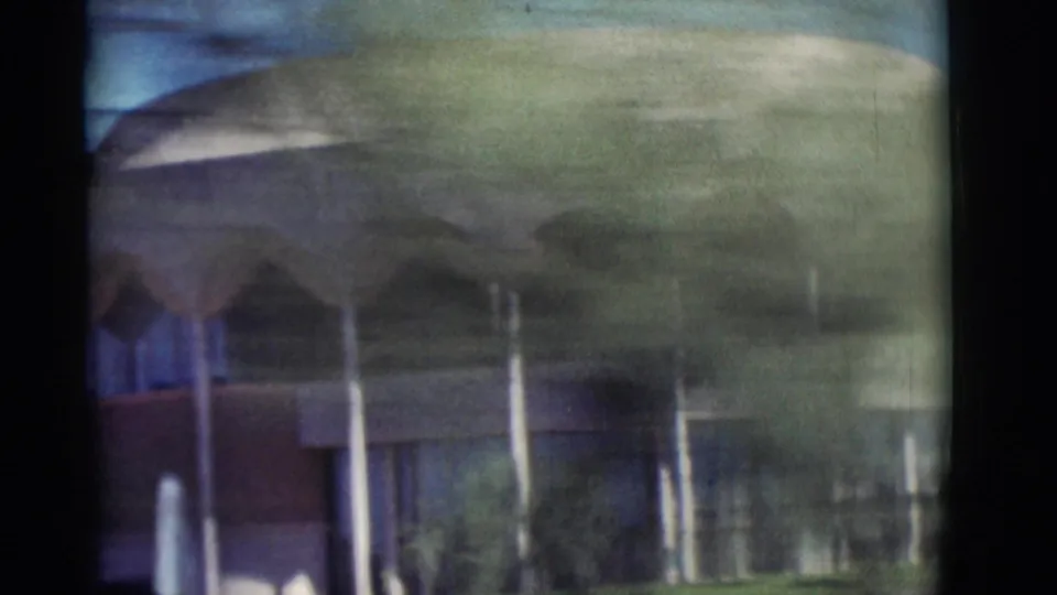 1964 New Mexico road-trip frame showing a modernist building with arched details, lawn, and heavy motion blur from a passing car.