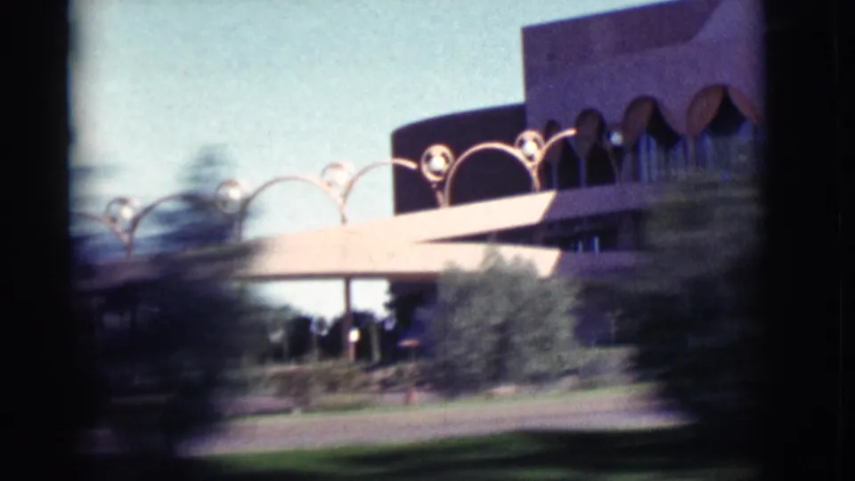 1964 New Mexico home-movie view of a modernist roadside building with arched forms, shrubs, lawn, and motion-softened foreground.