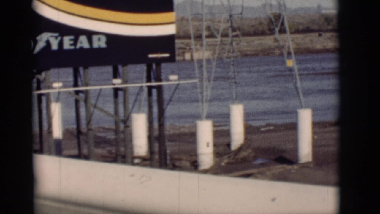 Goodyear sign above white posts with river water and dry landscape behind it.