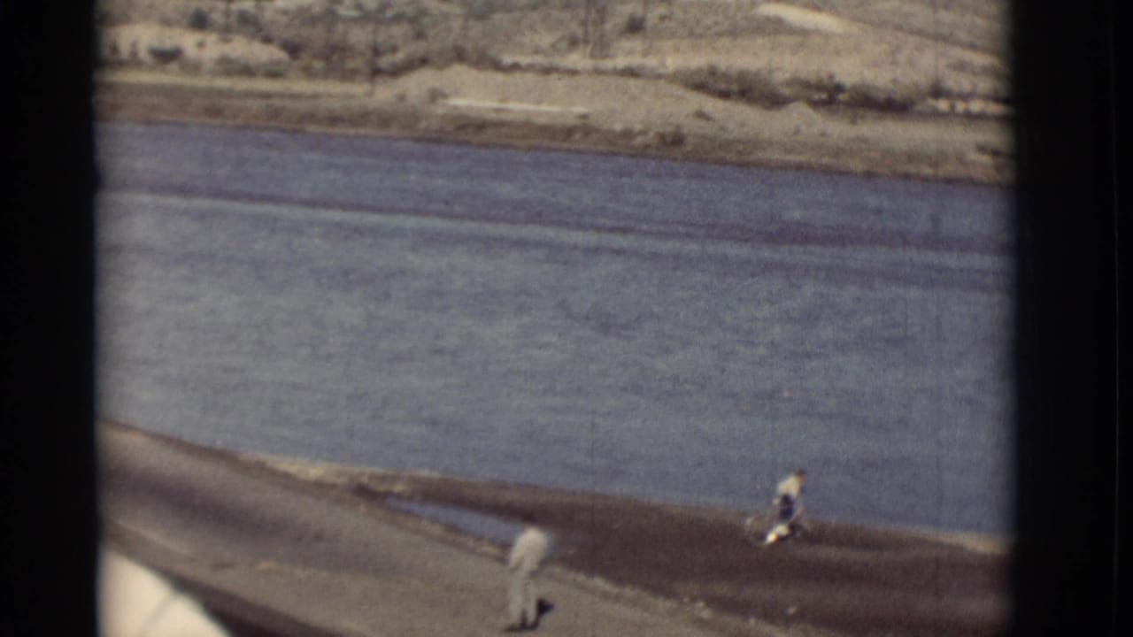 Riverbank road with one person walking and another riding a bicycle near the water.