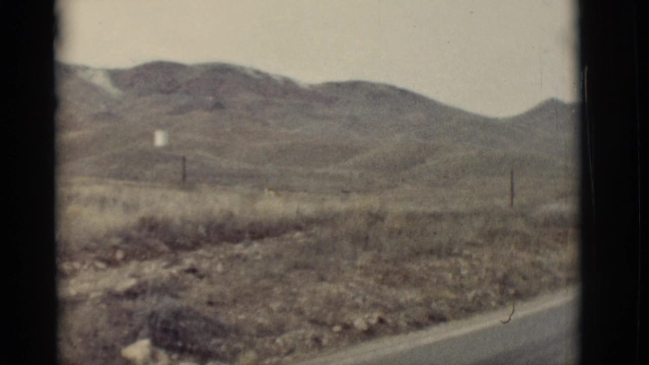 Desert hills beyond a rural road with dry grass and utility poles.