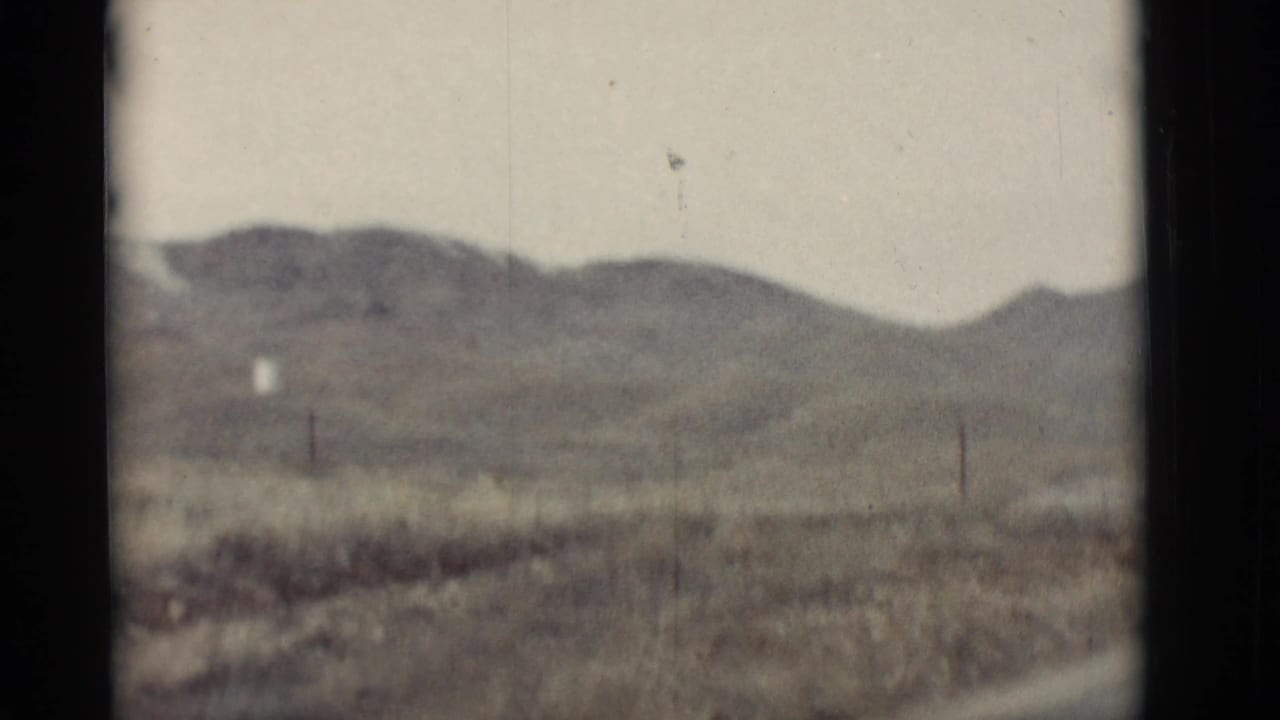 Blurred desert hillside landscape seen past a roadside foreground.
