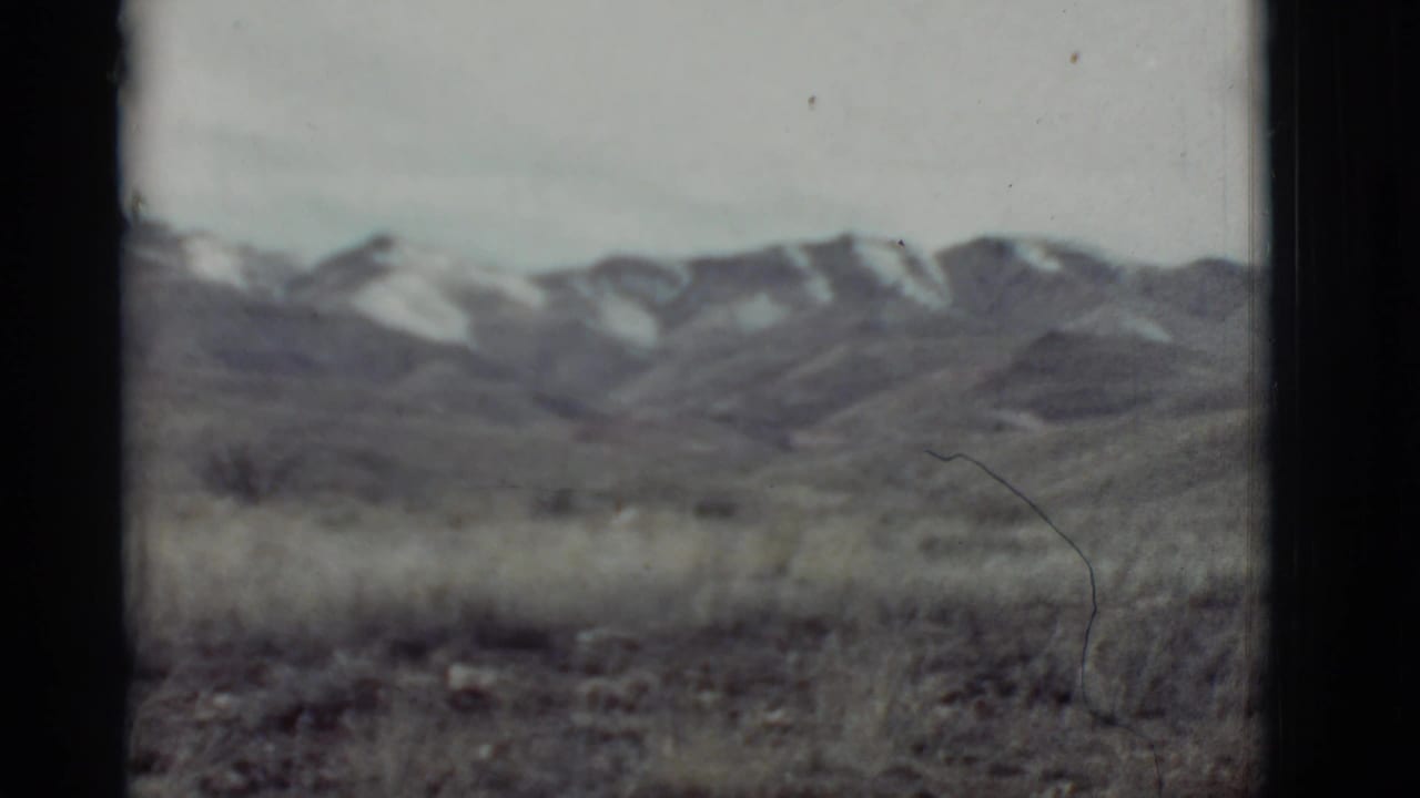 Distant snow-capped mountains beyond a grassy plain, seen through dark 8mm frame edges.