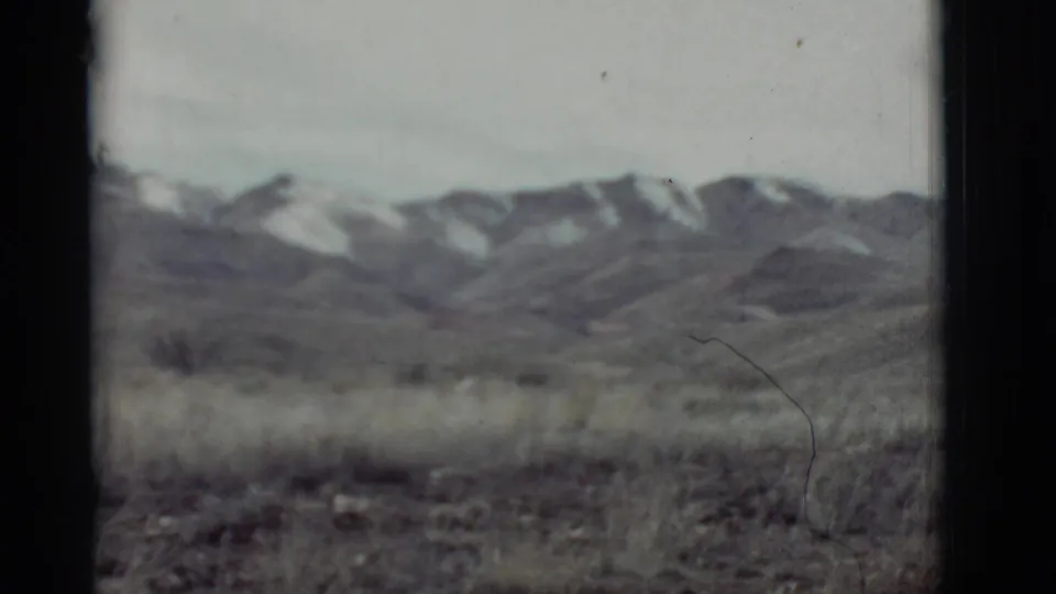 1964 New Mexico 8mm view of a dry grassy plain with distant snow-dusted mountain ridges under a pale sky.