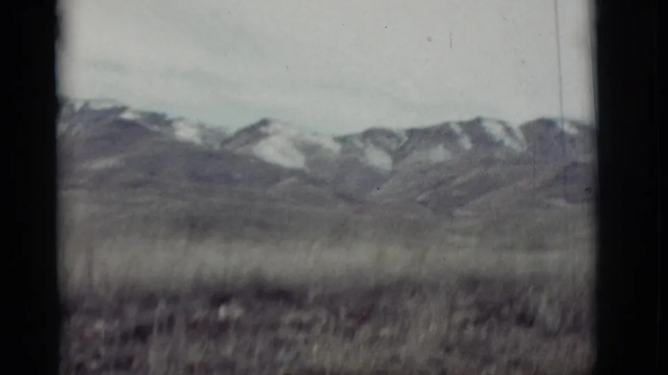 A 1964 New Mexico home-movie frame shows distant snowy mountains across a soft, grassy foreground.