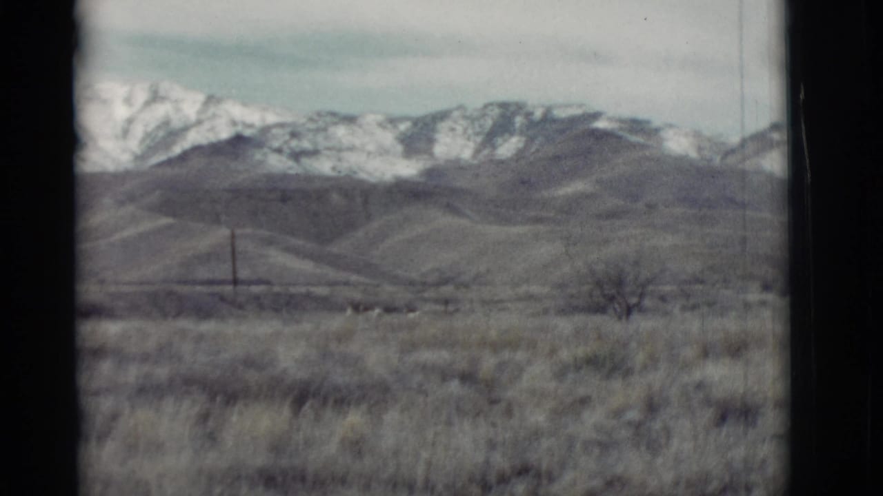 Dry grassland with rolling hills and snow-covered mountains in the distance.