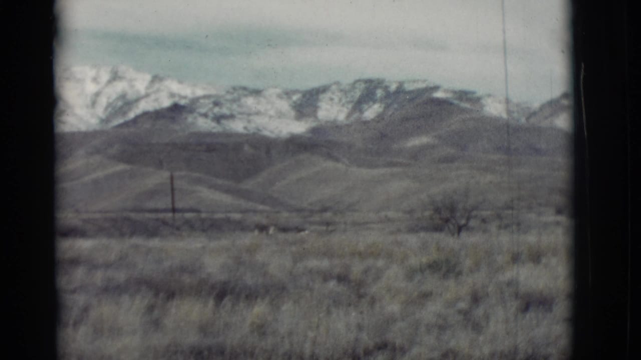 Snowy mountain range beyond low rolling hills and dry foreground grass.