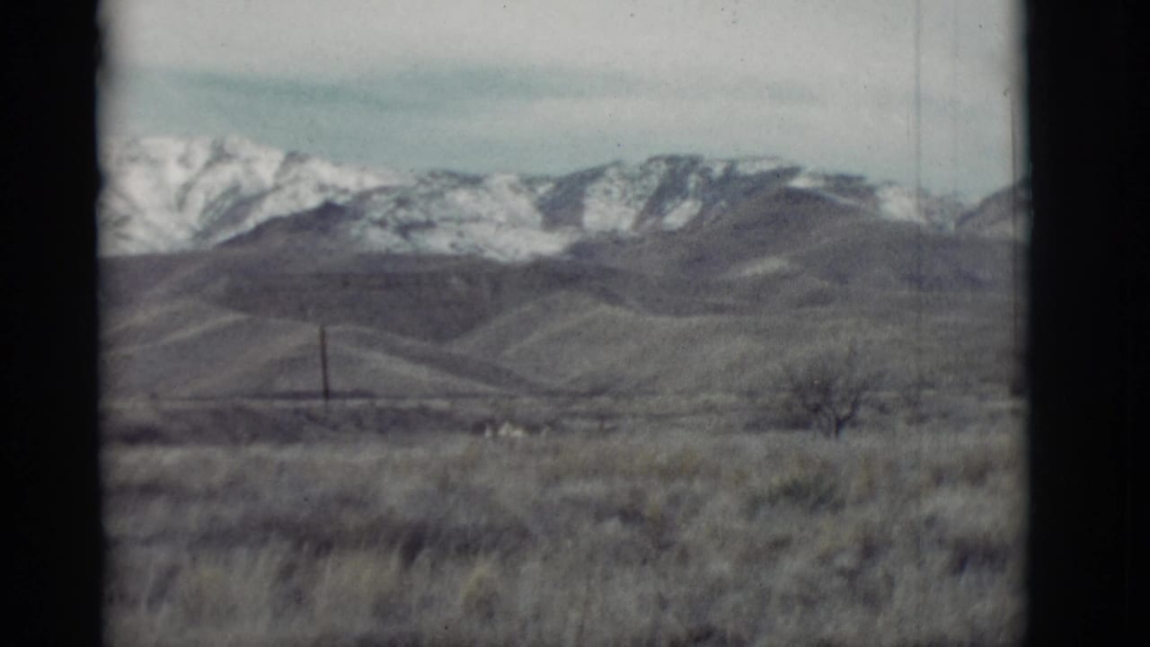 Dry field and rolling hills with snow-capped mountains in the distance.