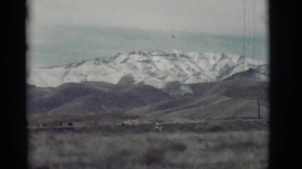 A small deer appears in a New Mexico field beneath snow-capped mountains in this 1964 8mm home-movie frame.