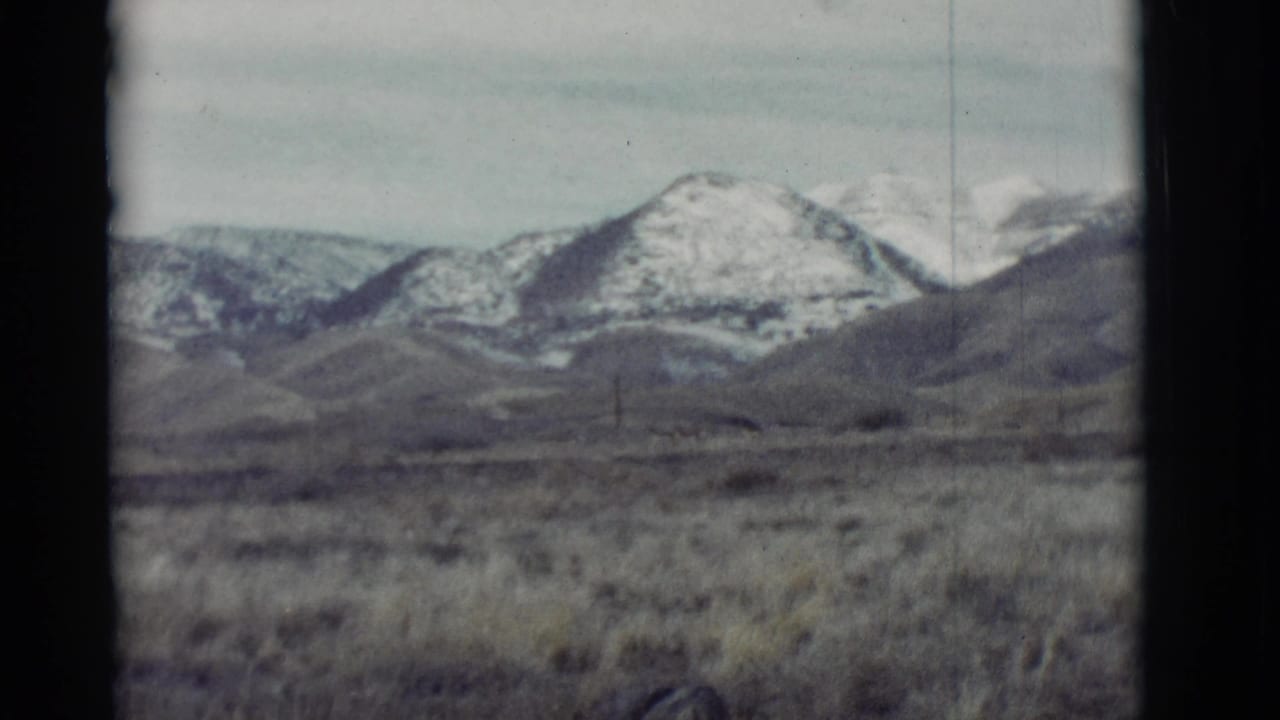 Distant mountain ridge and grassland seen inside a dark film frame.