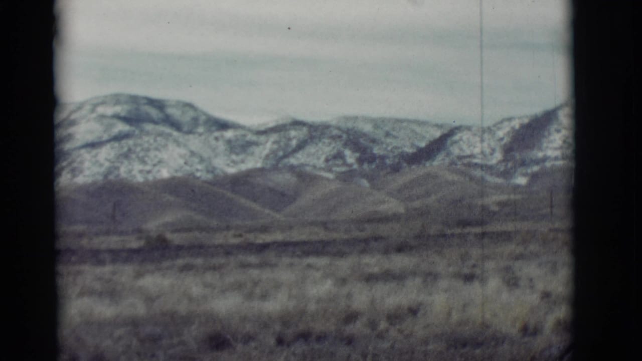 Dry grassland and low hills with snow-dusted mountains under a pale sky.