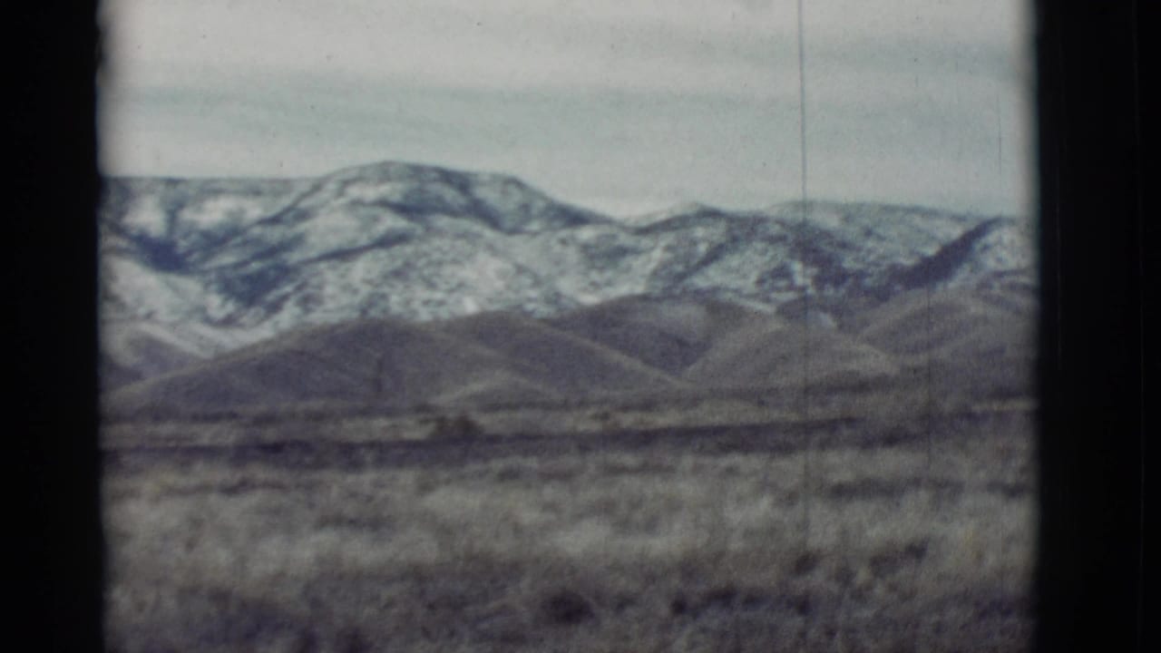Distant snow-streaked mountains beyond low desert hills and dry grass.